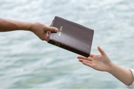 Two hands exchanging a Bible